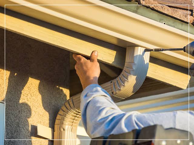Close-up of a downspout connection being secured beneath a gutter